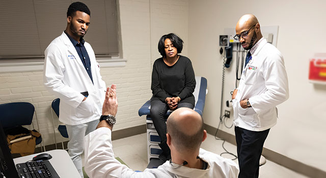 Duke students Rafeal Baker (left) and Nathaniel Neptune (right) listen as family nurse practitioner Virgil Mosu discusses a patient’s diagnosis 