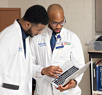 Students Rafeal Baker (left) and Nathaniel Neptune (right) review a patient’s chart before an exam.  