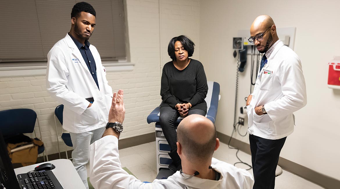 Duke Students Rafeal Baker (left) and Nathaniel Neptune (right) listen as family nurse practitioner Virgil Mosu discusses a patient’s diagnosis. 