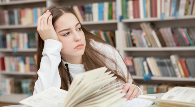 Teenage girl in library with book open, but looking away into the distance