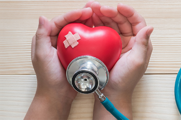 Heart with a band aid on it with stethoscope pressed to the bottom, held in cupped hands