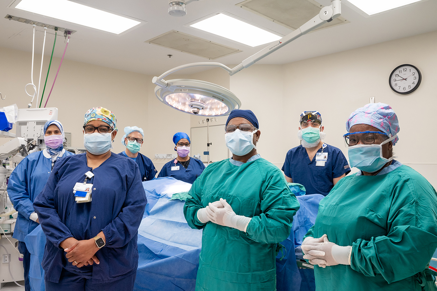 Employee Giving - A group of surgeons in full scrubs and masks stand around an operating room, posing for the camera. 