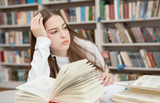 Teenage girl in library with book open, but looking away into the distance