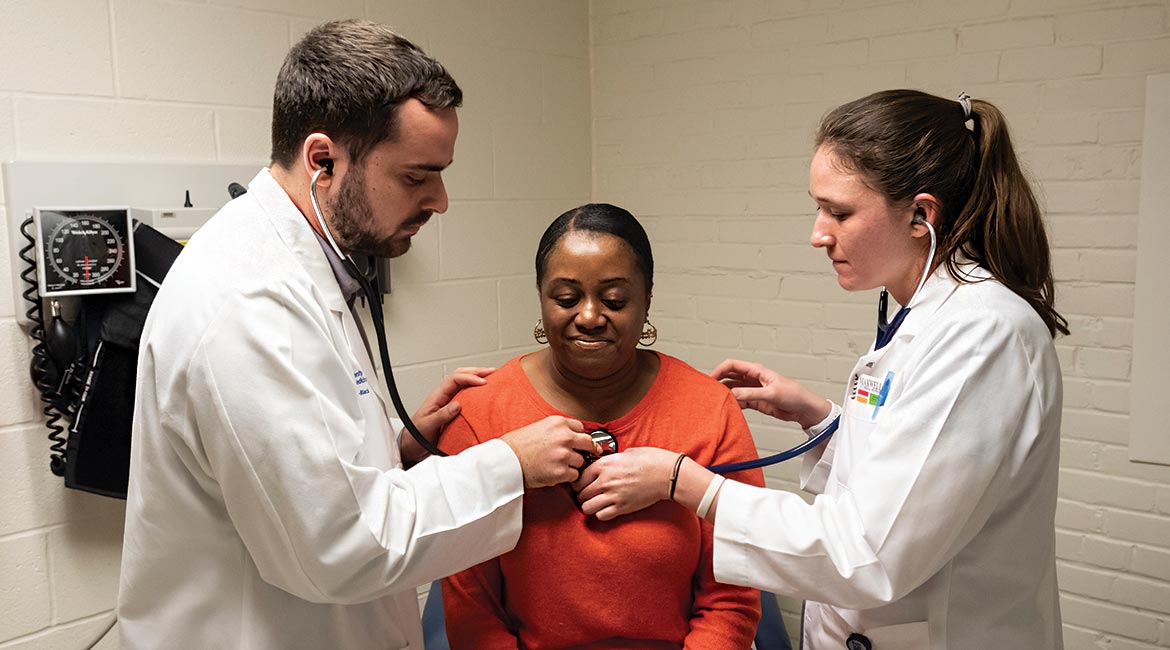 Peter Callejo-Black (left) guides fellow medical student Jenna Armstrong (right) through a patient exam.