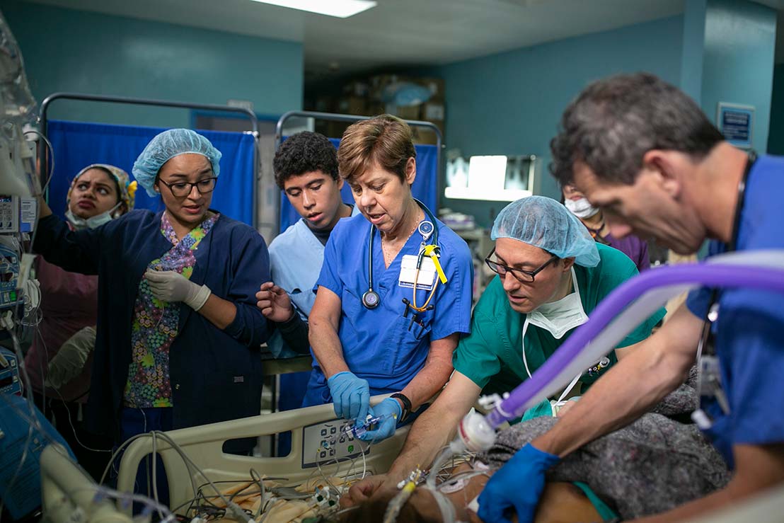 Following surgery, a patient is brought to the heart intensive care unit that the Duke team set up. Honduran nurse Waleska Flores, Duke's Myra Ellis, and Duke anesthesiologists J. Mauricio Del Rio and Joe DeBlasio monitor the patient with a translator.