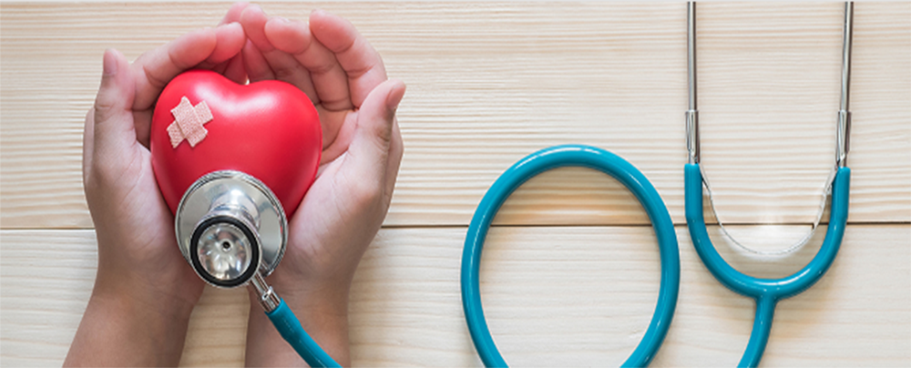 Heart with a band aid on it with stethoscope pressed to the bottom, held in cupped hands