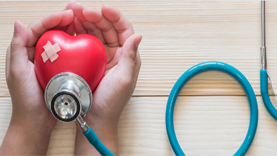 cupped hands holding a red heart with a bandaid and stethoscope on it. 