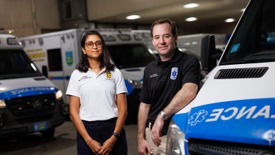 Andrew Godfrey, MD, and Anjni Joiner, DO, MPH in a garage surrounded by ambulances