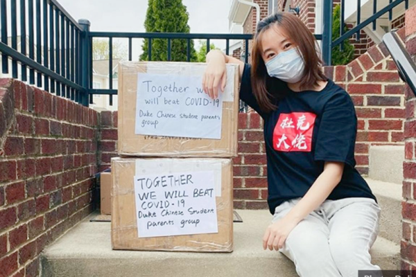 masked Chinese student with boxes of supplies 