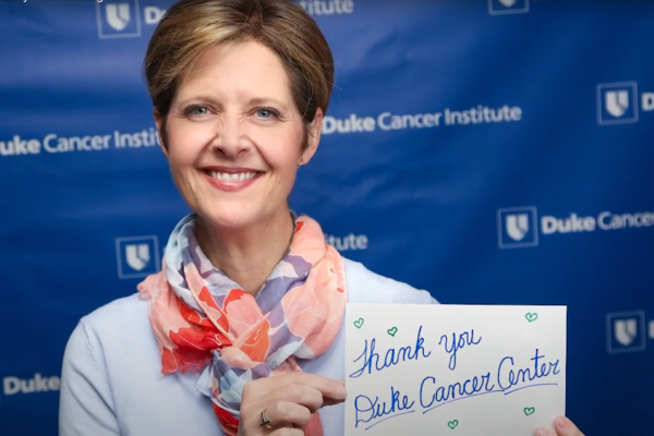 Tricia Gallagher holding up a card that says "thank you Duke Cancer Center"