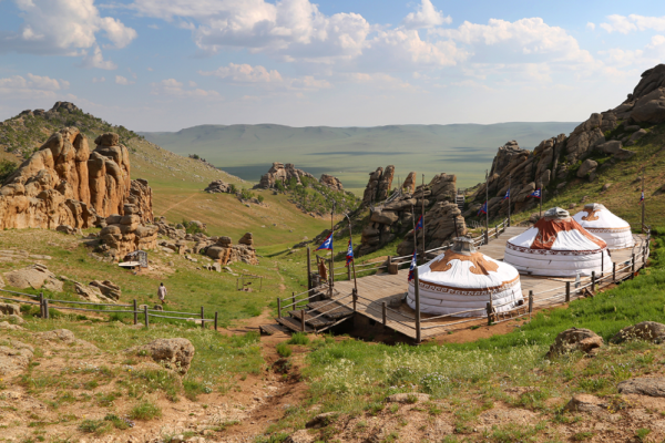 3 yurts in the foreground of a view of the hills and plains of Mongolia