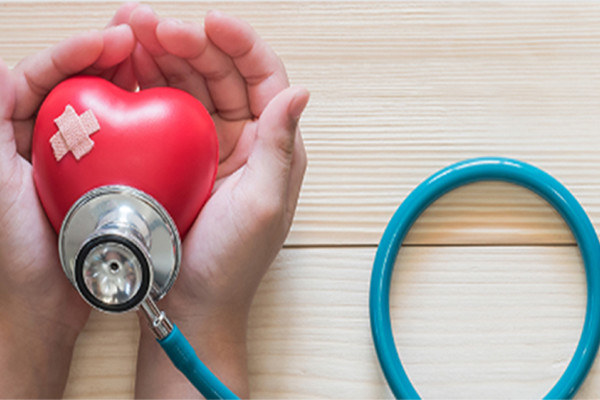 cupped hands holding a red heart with a bandaid and stethoscope on it. 