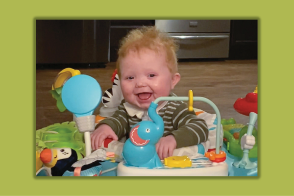 smiling baby in a play seat surrounded by colorful toys
