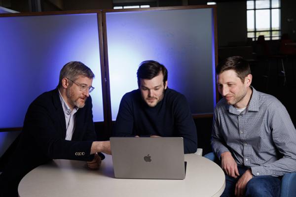 Drs. Jonathan Posner, Elliot Hill and Matthew Englehard look at a laptop computer  in a darkened room. The research team developed an AI model that helps predict mental illness in adolescents.