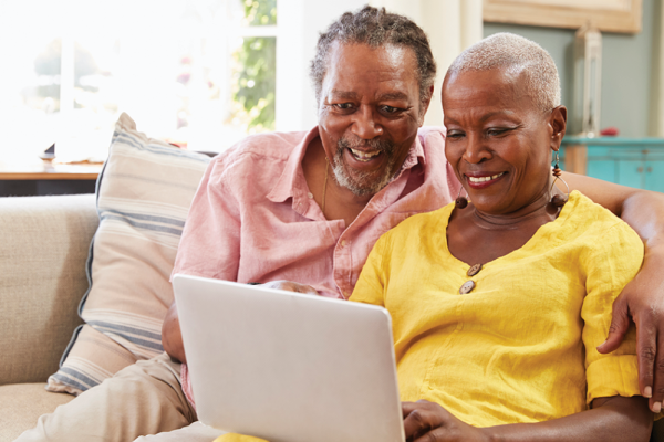 an older Black couple sitting together on a sofa sharing a laptop. 