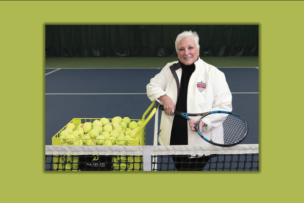 Donna Bernstein on a tennis court holding a racket next to a basket of tennis balls