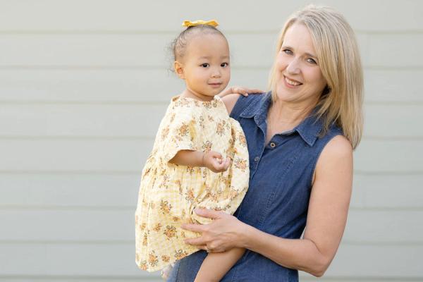 Darla holds Kara outside in front of the wall of a home