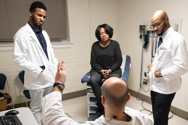 Duke Students Rafeal Baker (left) and Nathaniel Neptune (right) listen as family nurse practitioner Virgil Mosu discusses a patient’s diagnosis.