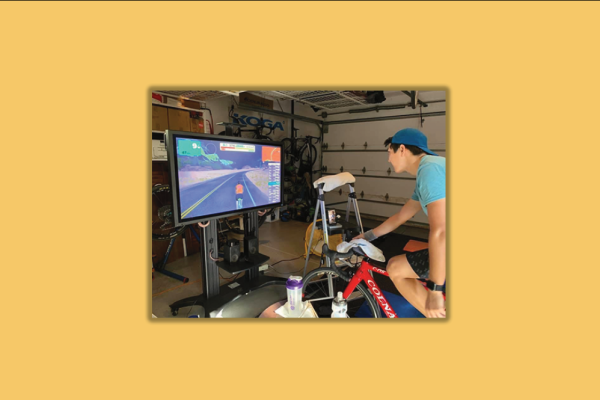 Justin Koga rides a bike in a garage facing a screen. 