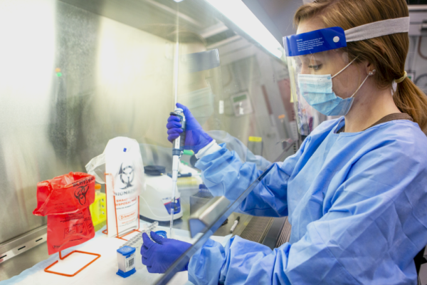 woman in full PPE pipetting under a hood