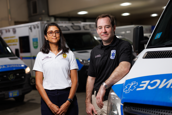 Andrew Godfrey, MD, and Anjni Joiner, DO, MPH in a garage surrounded by ambulances