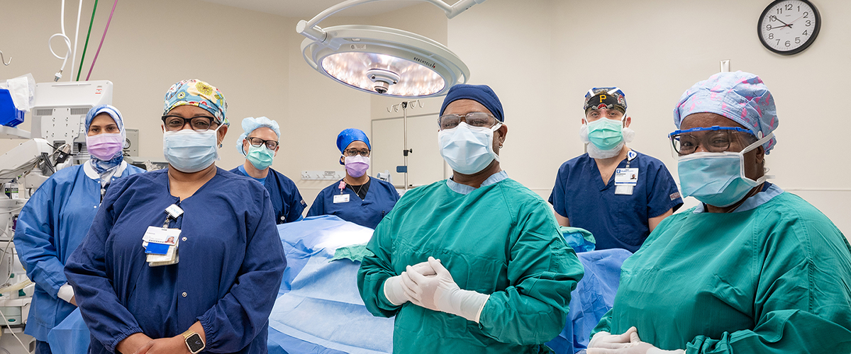 A group of surgeons in full scrubs and masks standing in an operating room, posing for the camera. 