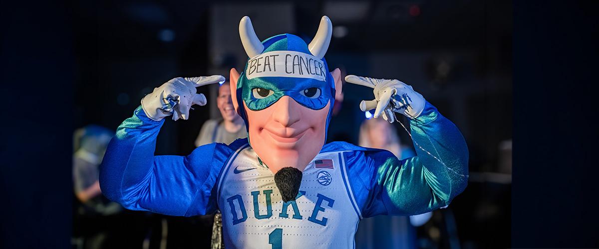 the duke blue devil mascot point to the words "beat cancer" written on his head