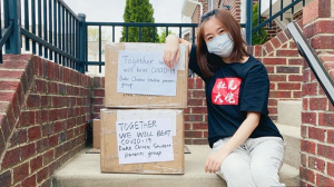 masked Chinese student with boxes of supplies 