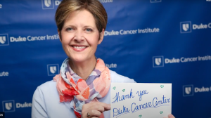 Tricia Gallagher holding up a card that says "thank you Duke Cancer Center"