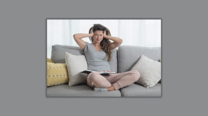 woman sitting on a sofa covering her ears as if a noise hurts her hears. 