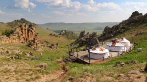 3 yurts in the foreground of a view of the hills and plains of Mongolia