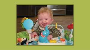 smiling baby in a play seat surrounded by colorful toys