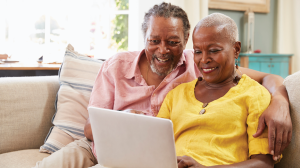 an older Black couple sitting together on a sofa sharing a laptop. 