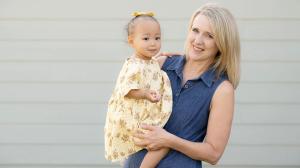 Darla holds Kara outside in front of the wall of a home