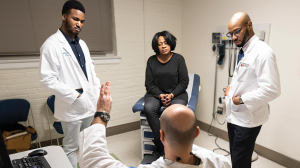 Duke Students Rafeal Baker (left) and Nathaniel Neptune (right) listen as family nurse practitioner Virgil Mosu discusses a patient’s diagnosis.