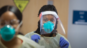 Black woman healthcare worker in PPE preparing to care for patients. 