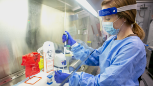woman in full PPE pipetting under a hood