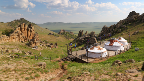 3 yurts in the foreground of a view of the hills and plains of Mongolia