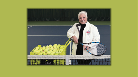 Donna Bernstein on a tennis court holding a racket next to a basket of tennis balls