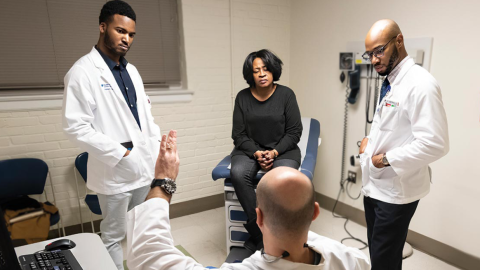 Duke Students Rafeal Baker (left) and Nathaniel Neptune (right) listen as family nurse practitioner Virgil Mosu discusses a patient’s diagnosis.