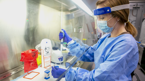 woman in full PPE pipetting under a hood