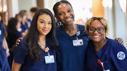 Three students in scrubs standing together and smiling