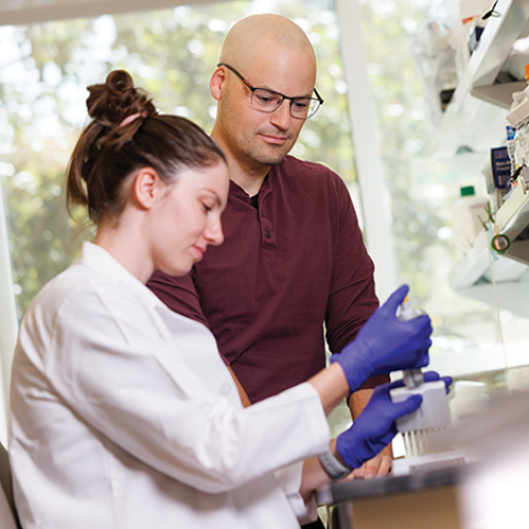 woman in a lab coat next to a man in a red shirt working in a lab