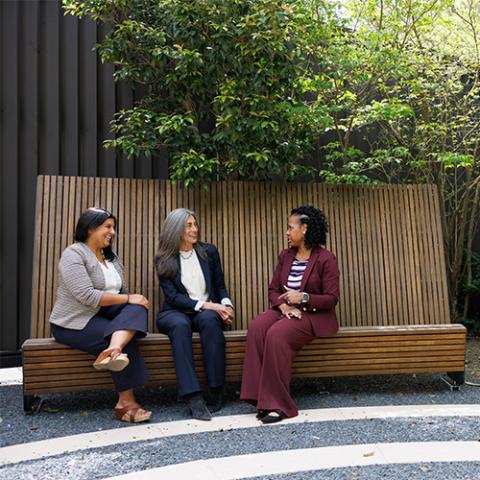 three women sitting on a bench having a discussion