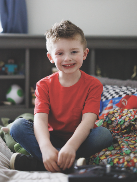 a smiling child sitting on his bed