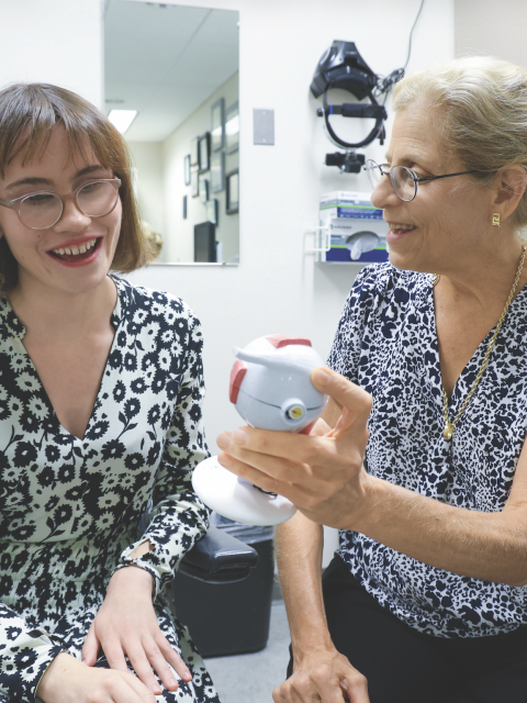 A patient and provider interacting in a clinical room. The provider is holding out an medical instrument.