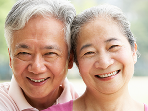 Older Asian couple, heads together, smiling into the camera