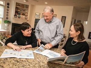 Bill and Meg Lindenberger and their adult daughter Kim sitting at a table reading a newspaper
